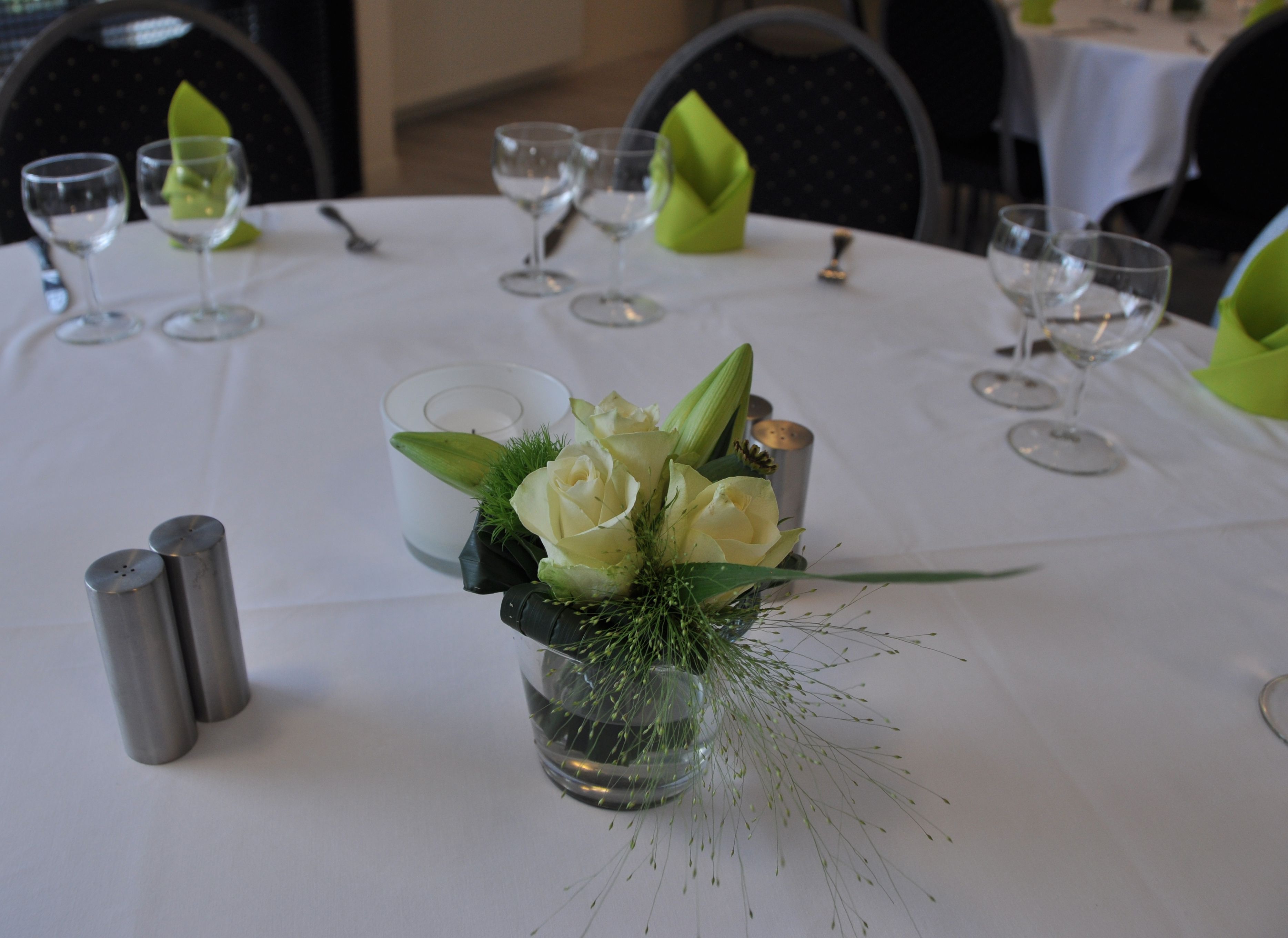 Een gedekte tafel voor een formeel diner, met een middelpunt van witte rozen en groen, zout- en peperstel en wijnglazen.