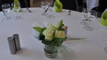 Een gedekte tafel voor een formeel diner, met een middelpunt van witte rozen en groen, zout- en peperstel en wijnglazen.