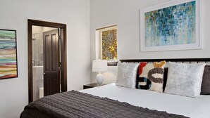 A hotel room with a bed, a nightstand, a lamp, a painting, and a window with a view of trees. - Timberfalls 1905 3 Bedroom Condo by RedAwning (Vail)