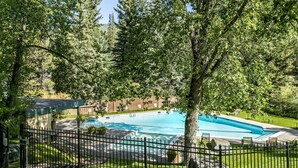 A swimming pool surrounded by a fence, with a grassy area and trees in the background. - Timberfalls 1905 3 Bedroom Condo by RedAwning (Vail)