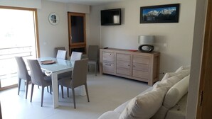 A modern living room with a dining area, a sofa, a TV, and a painting on the wall.