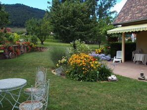 A garden with a patio area, a metal table and chairs, and a small building with a tiled roof.