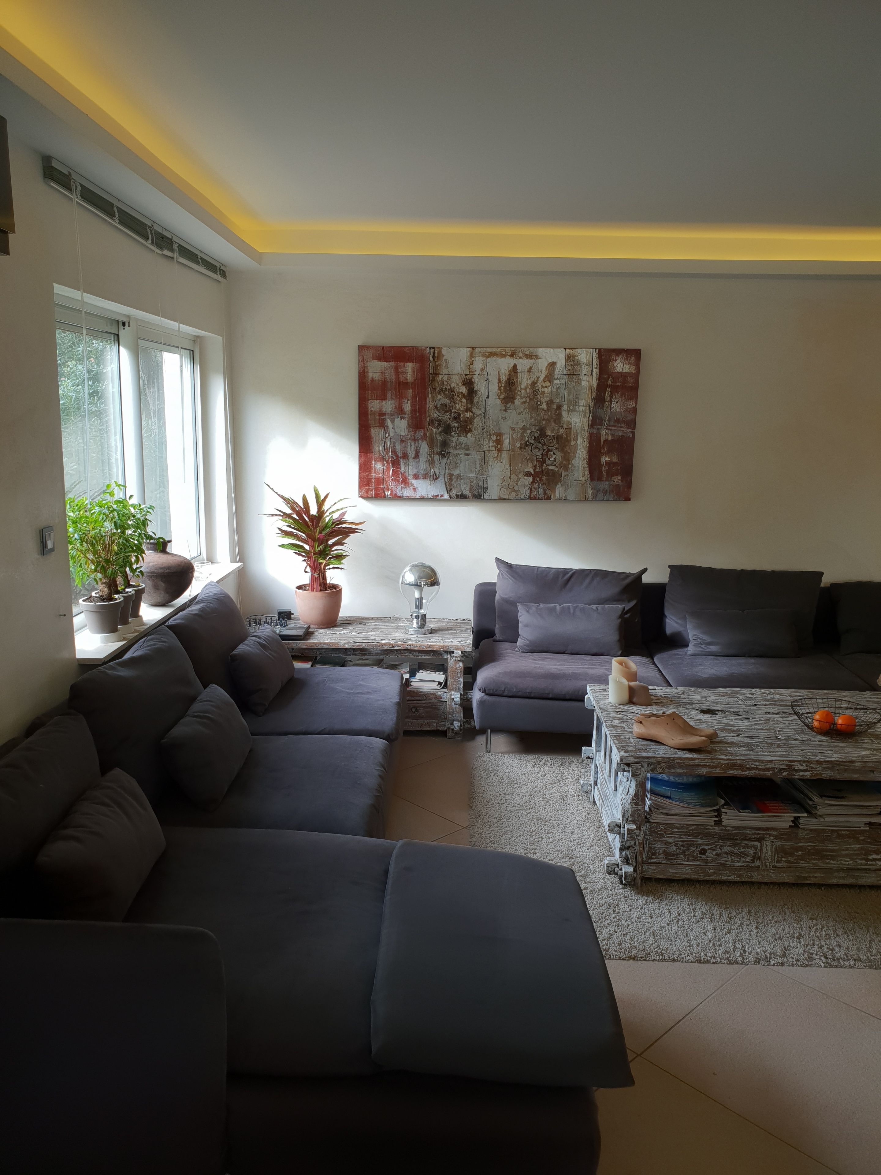 Una sala moderna con un sofá seccional gris, una mesa de centro y un cuadro abstracto grande en la pared.