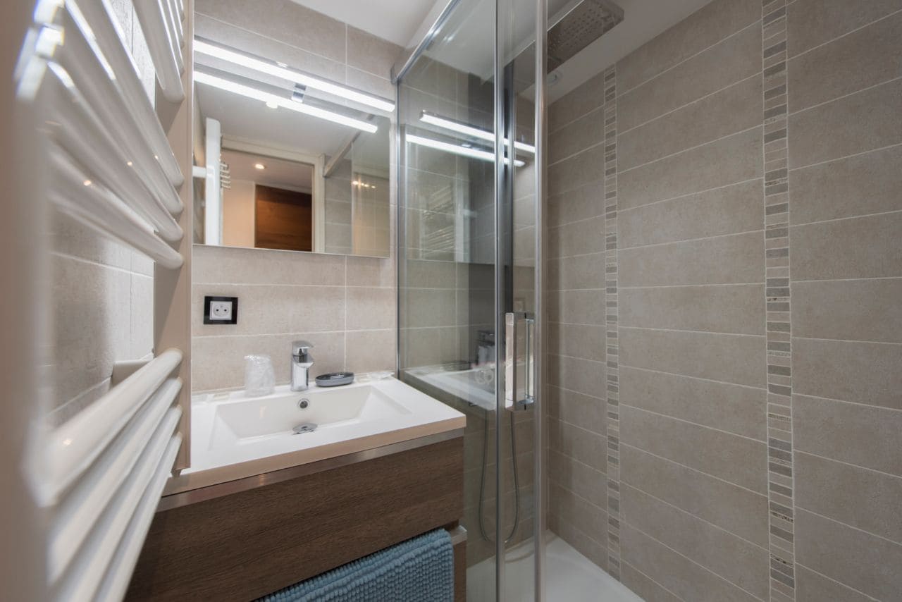 Une salle de bain moderne avec une douche à parois de verre, un lavabo blanc et un meuble-lavabo en bois.