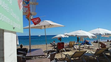 Una playa con tumbonas y sombrillas, un cartel con logotipo de corazón y un cielo azul despejado.