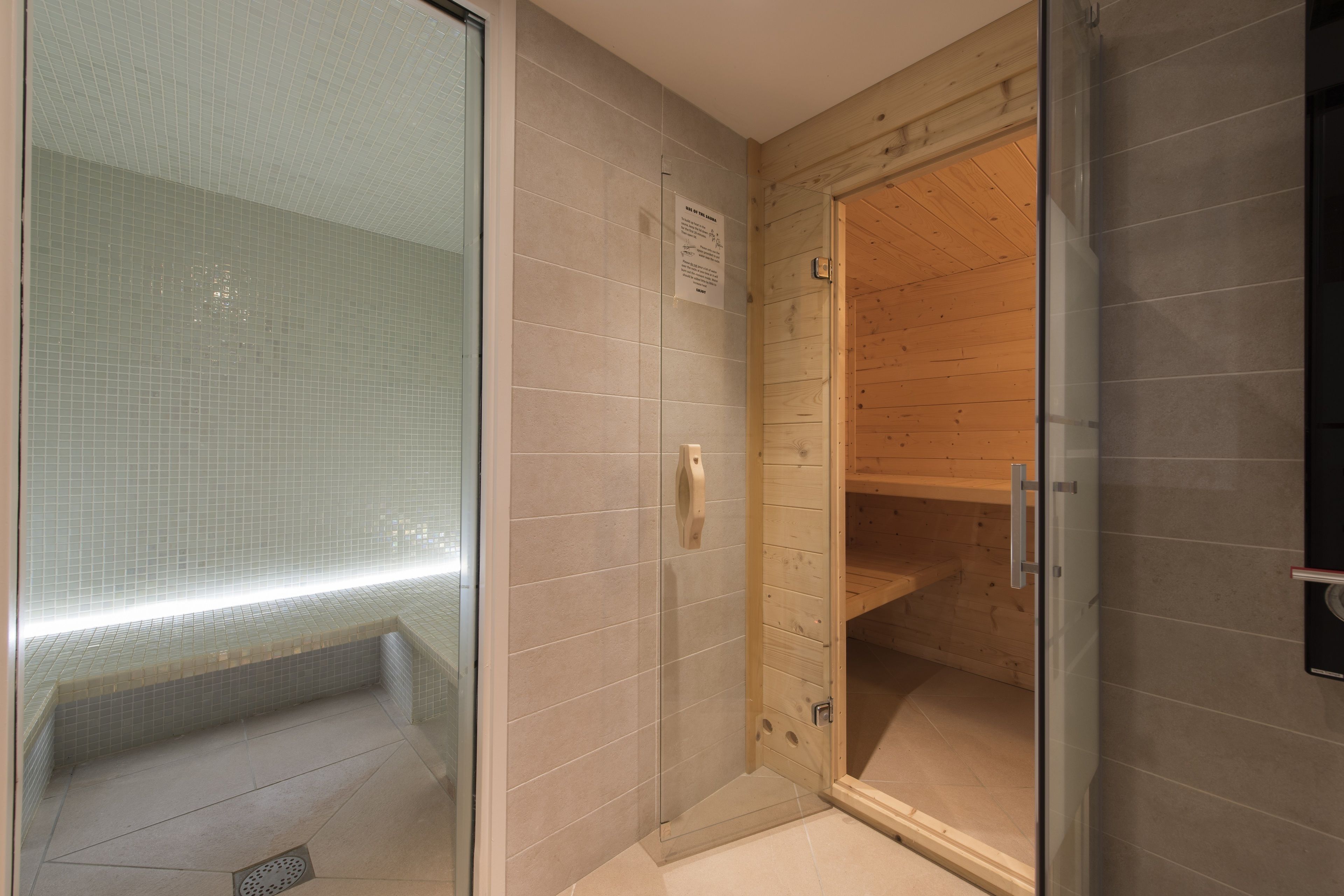 Un baño moderno con cabina de ducha de vidrio, paredes alicatadas y un banco de madera.