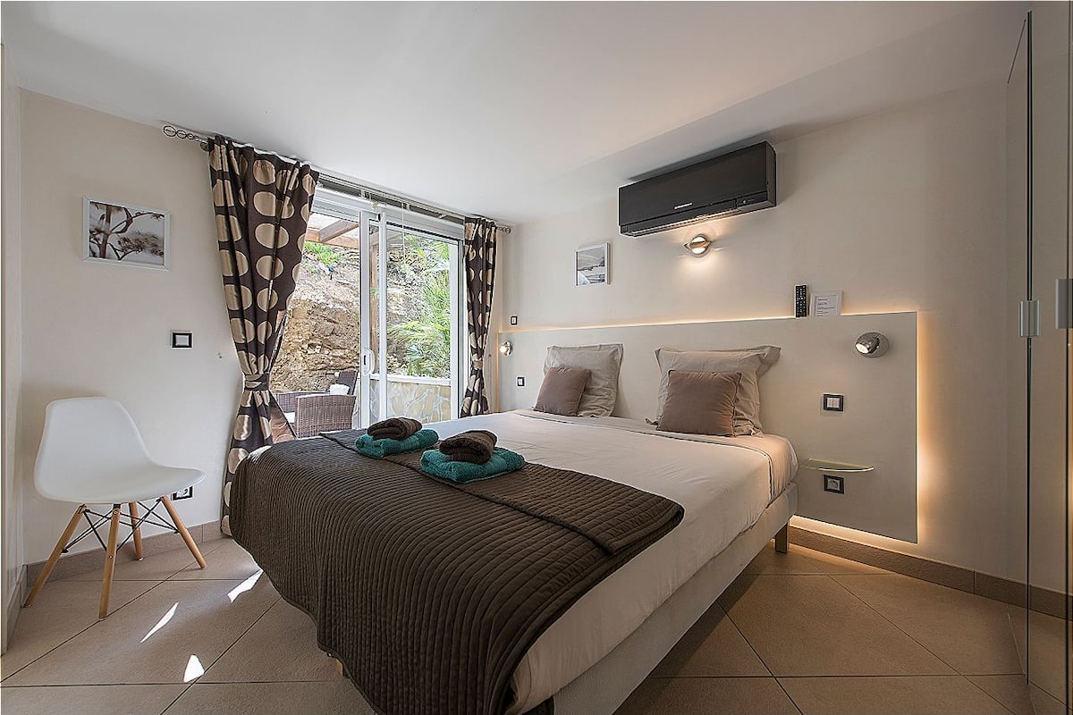 Une chambre moderne avec un grand lit, un téléviseur à écran plat fixé au-dessus du lit et une vue sur l’extérieur grâce à une porte-fenêtre coulissante.