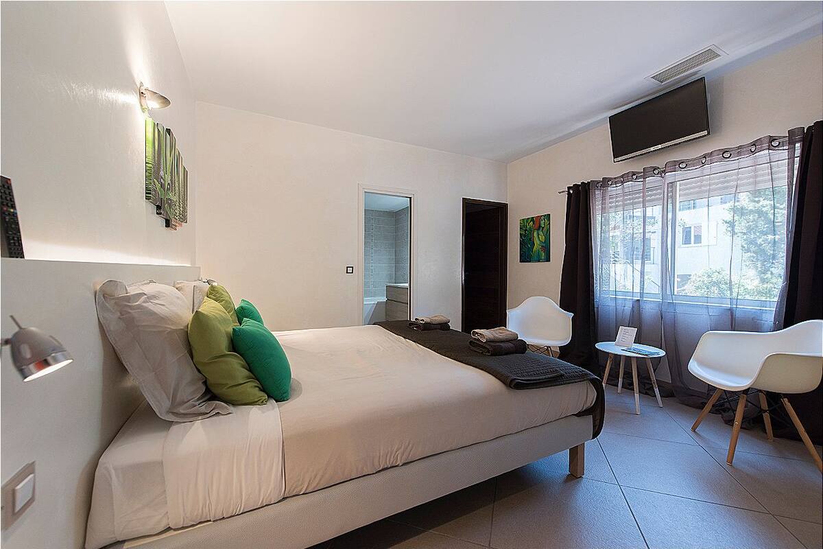 Une chambre d’hôtel avec un lit, une télévision, une petite table, deux chaises et une fenêtre avec des rideaux.