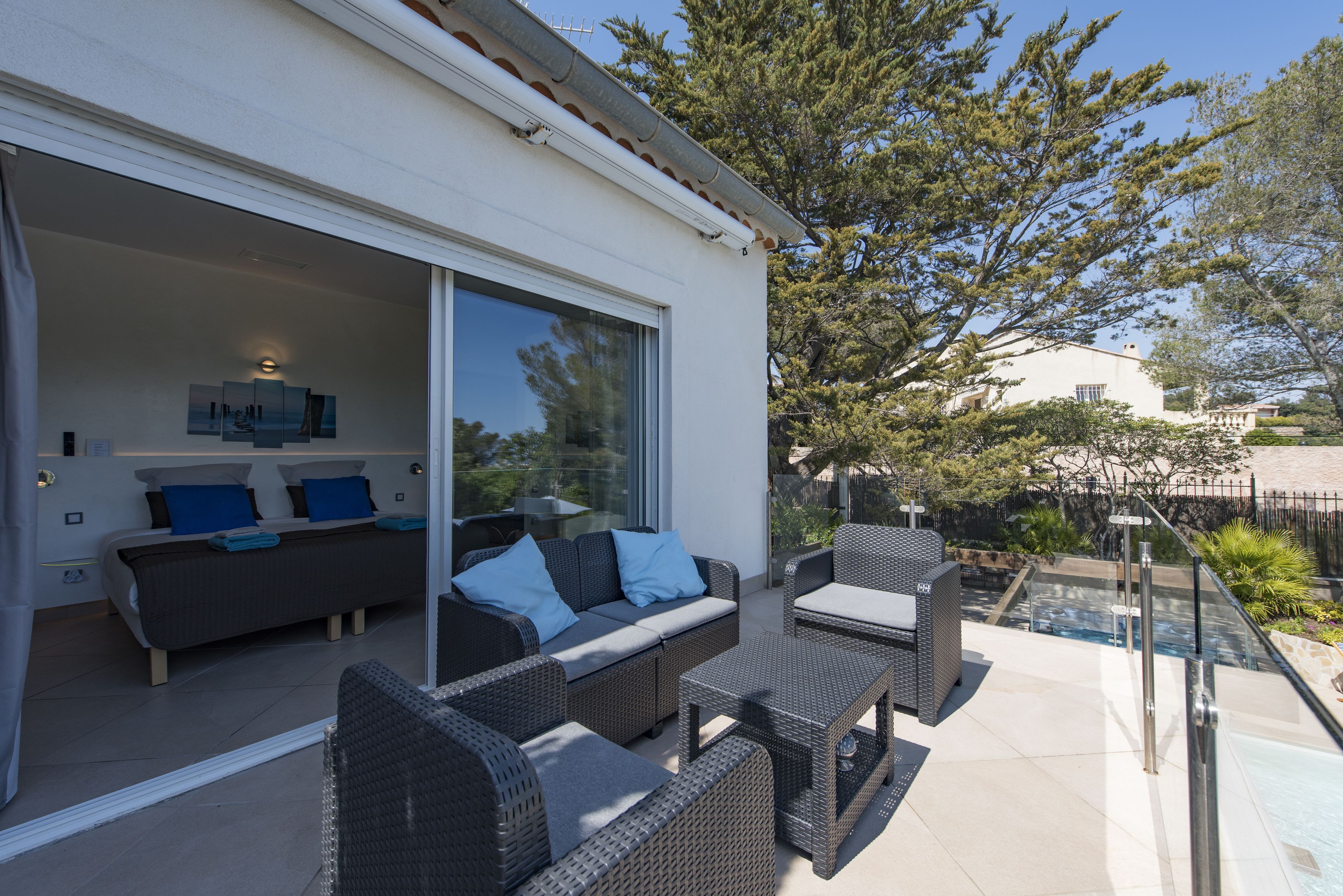 A modern outdoor living area with a sofa and chairs, a pool, and a glass door leading to a bedroom.