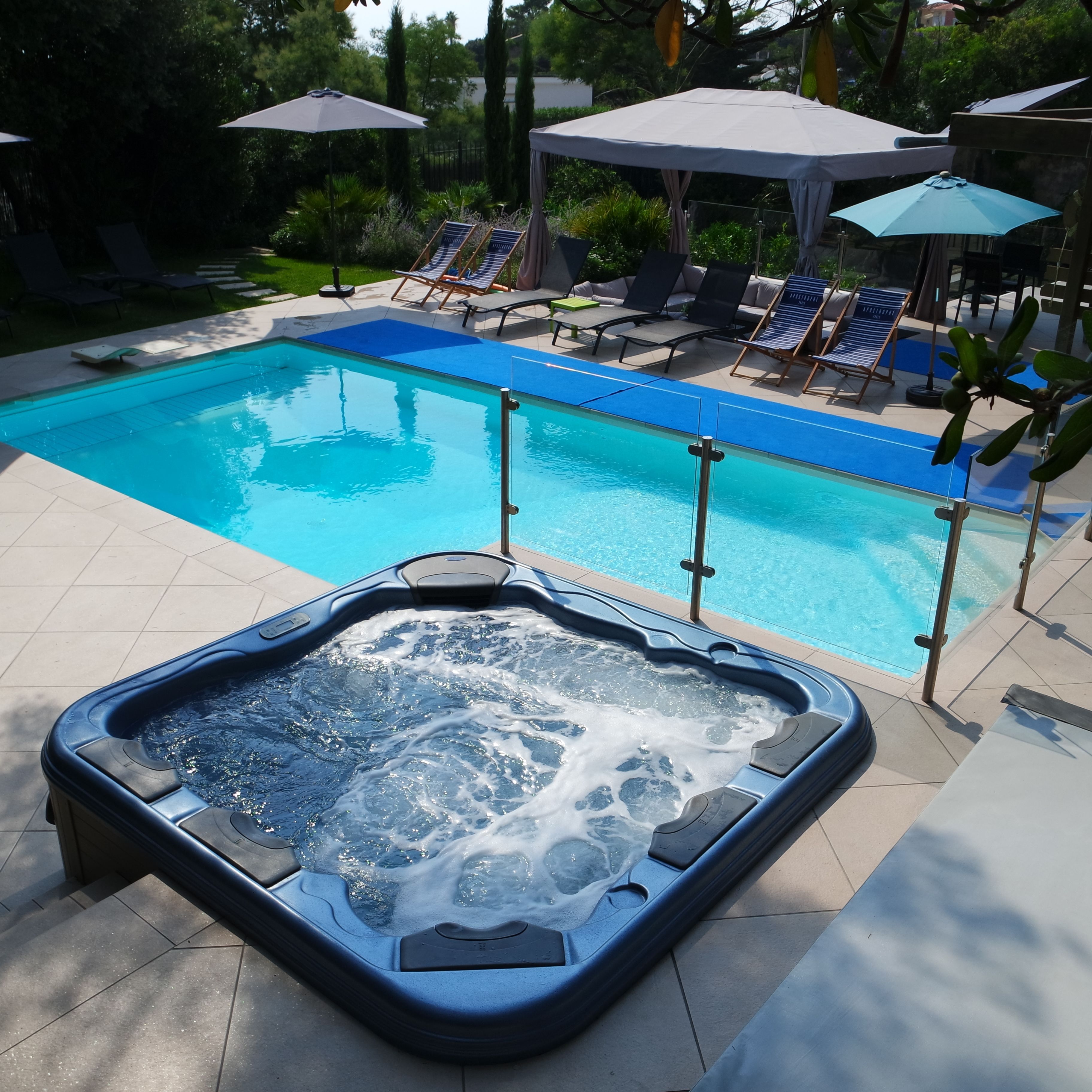 Une piscine avec des chaises longues et des parasols, et un jacuzzi au premier plan.