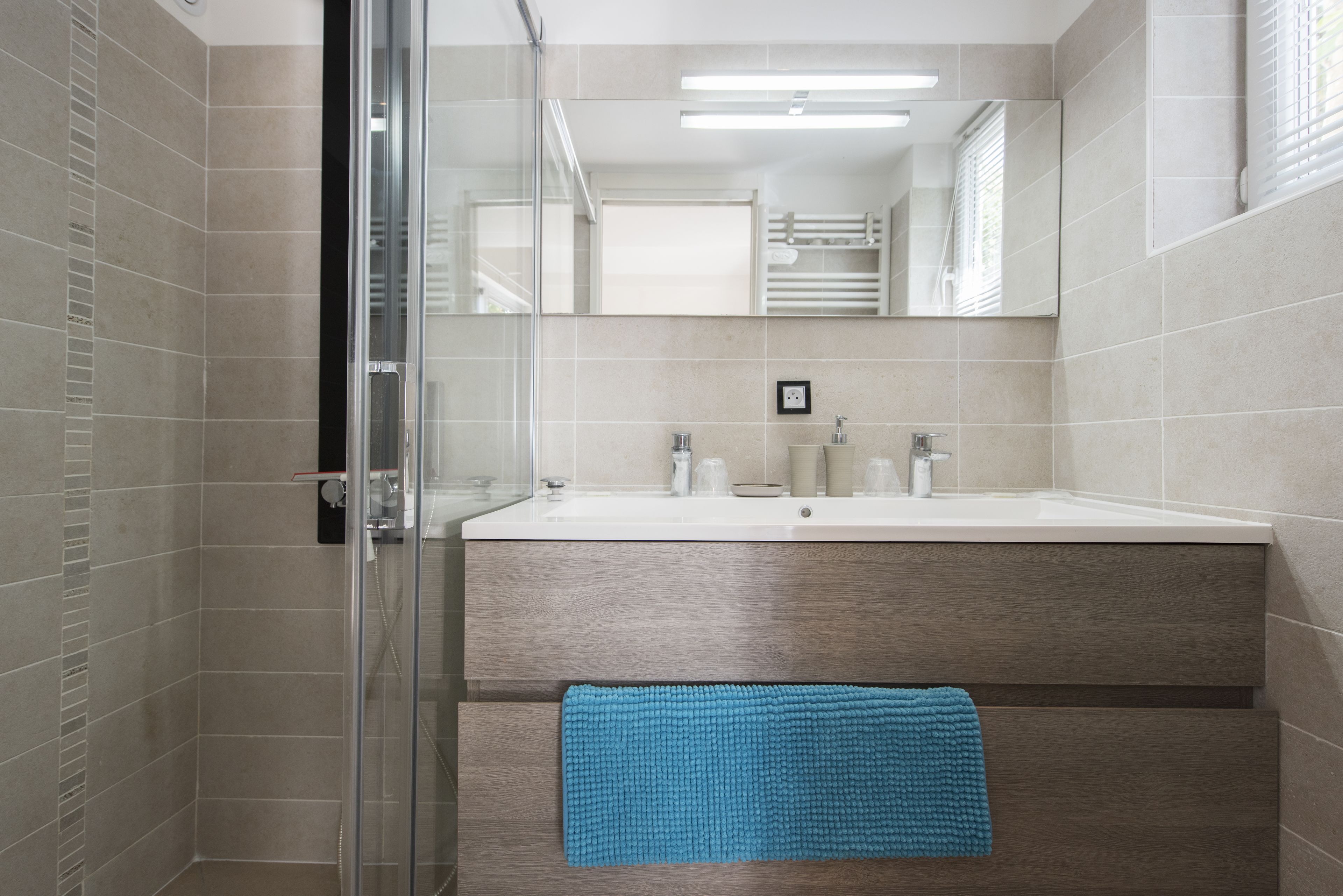 Ein modernes Badezimmer mit Duschkabine aus Glas, einem Holzwaschtisch und einem blauen Handtuch an der Wand.