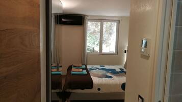 Un dormitorio con cama, ventana con vista a árboles, televisor de pared y termostato.