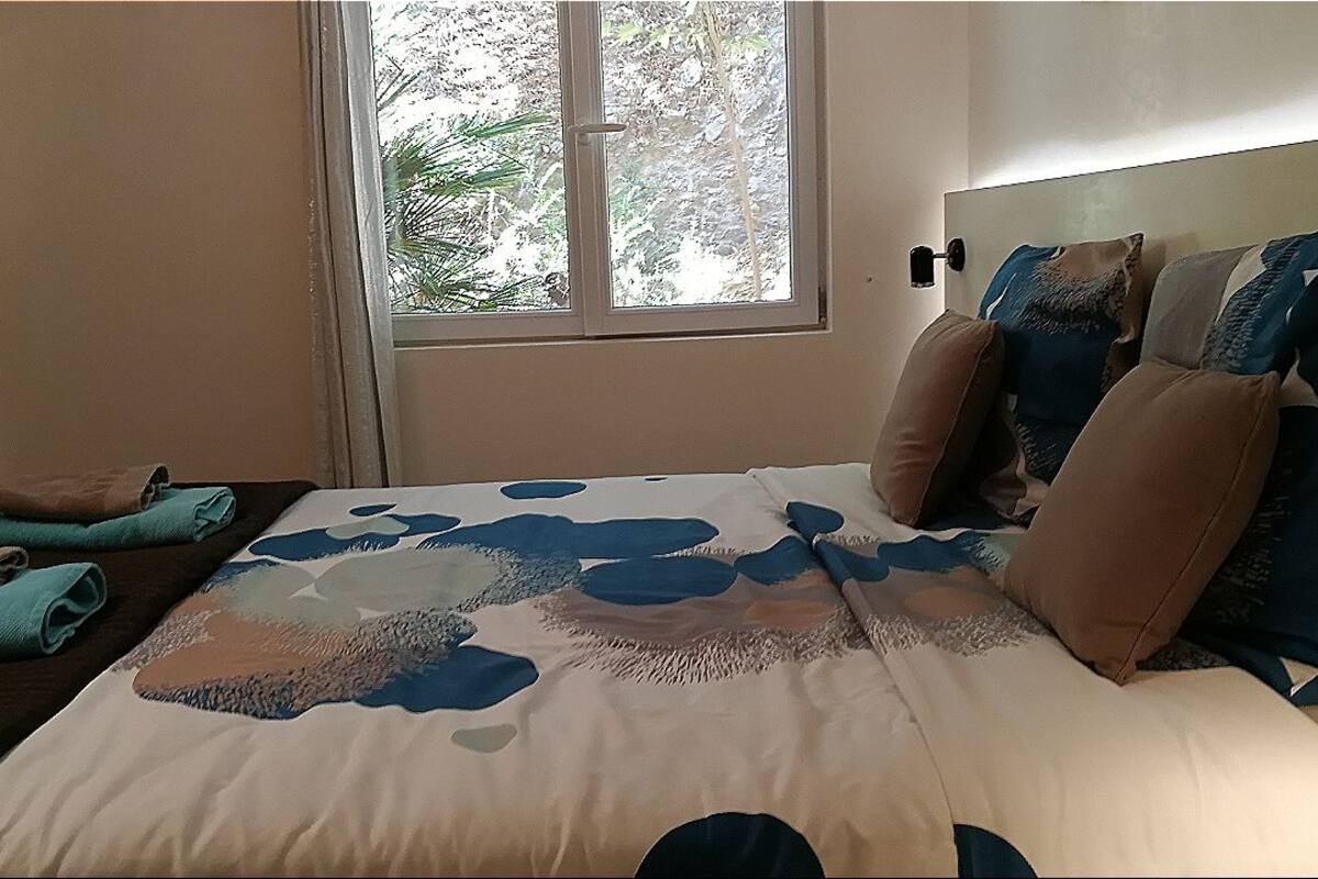 Une chambre à coucher avec un lit, des oreillers, une fenêtre et une table de chevet.