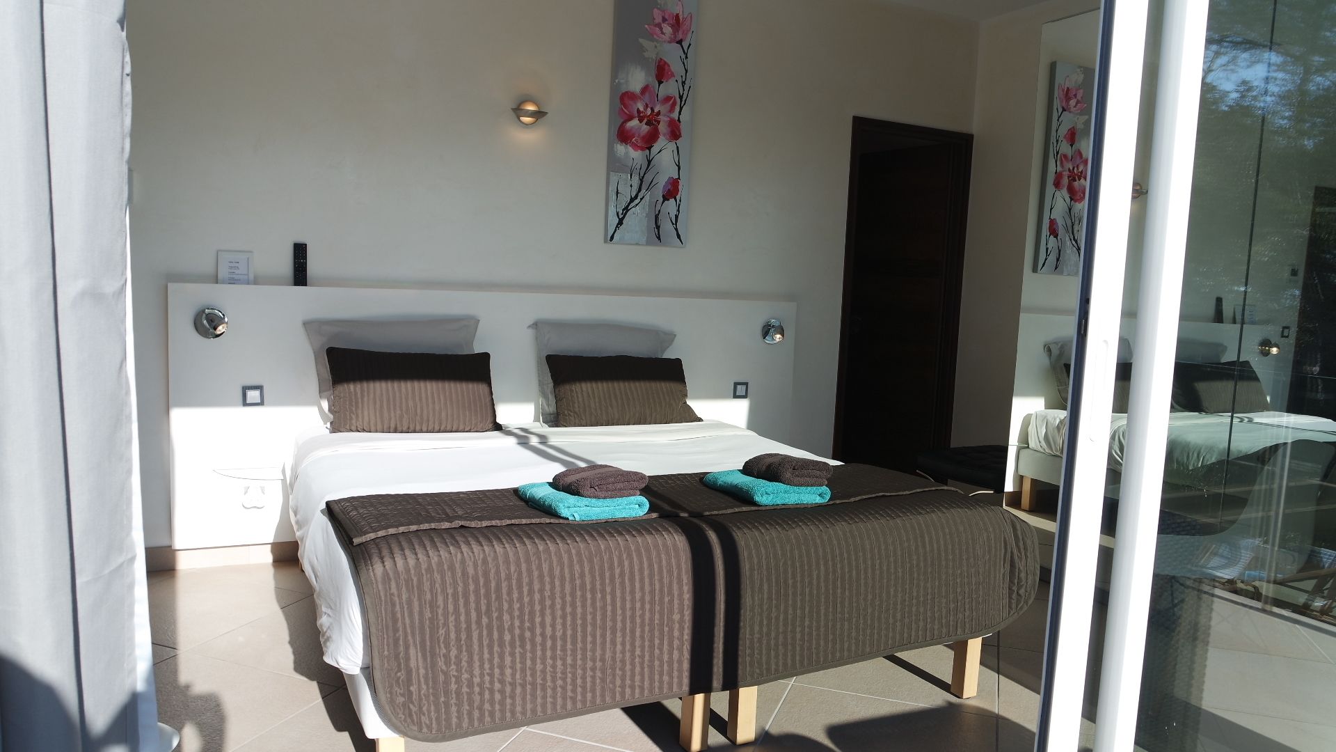 A modern bedroom with a large bed, two bedside tables, and a glass door leading to a balcony.