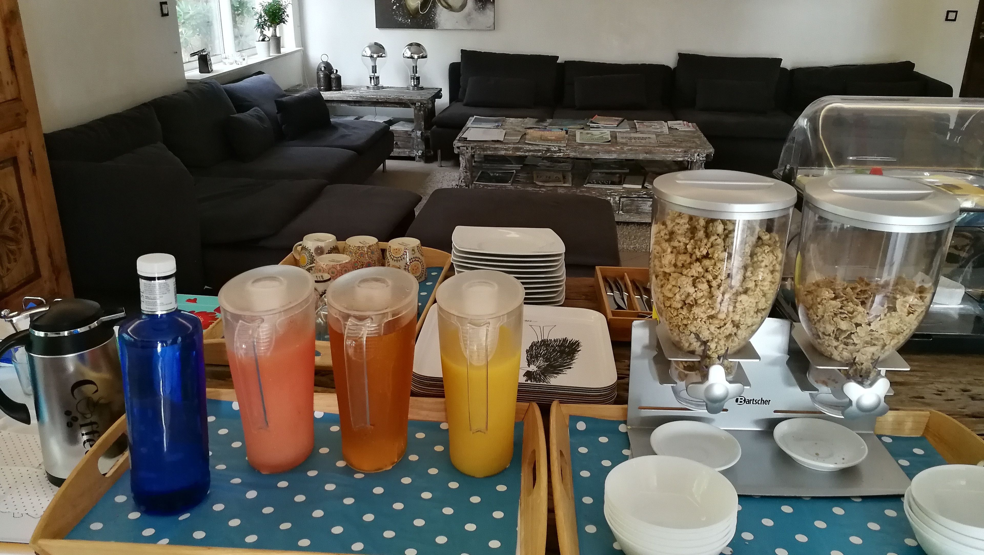 A living room with a coffee table, sofa, and a dining area with a buffet setup including drinks and food containers.