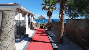 Camí que porta a una platja amb catifes vermelles, palmeres i una paret de pedra.