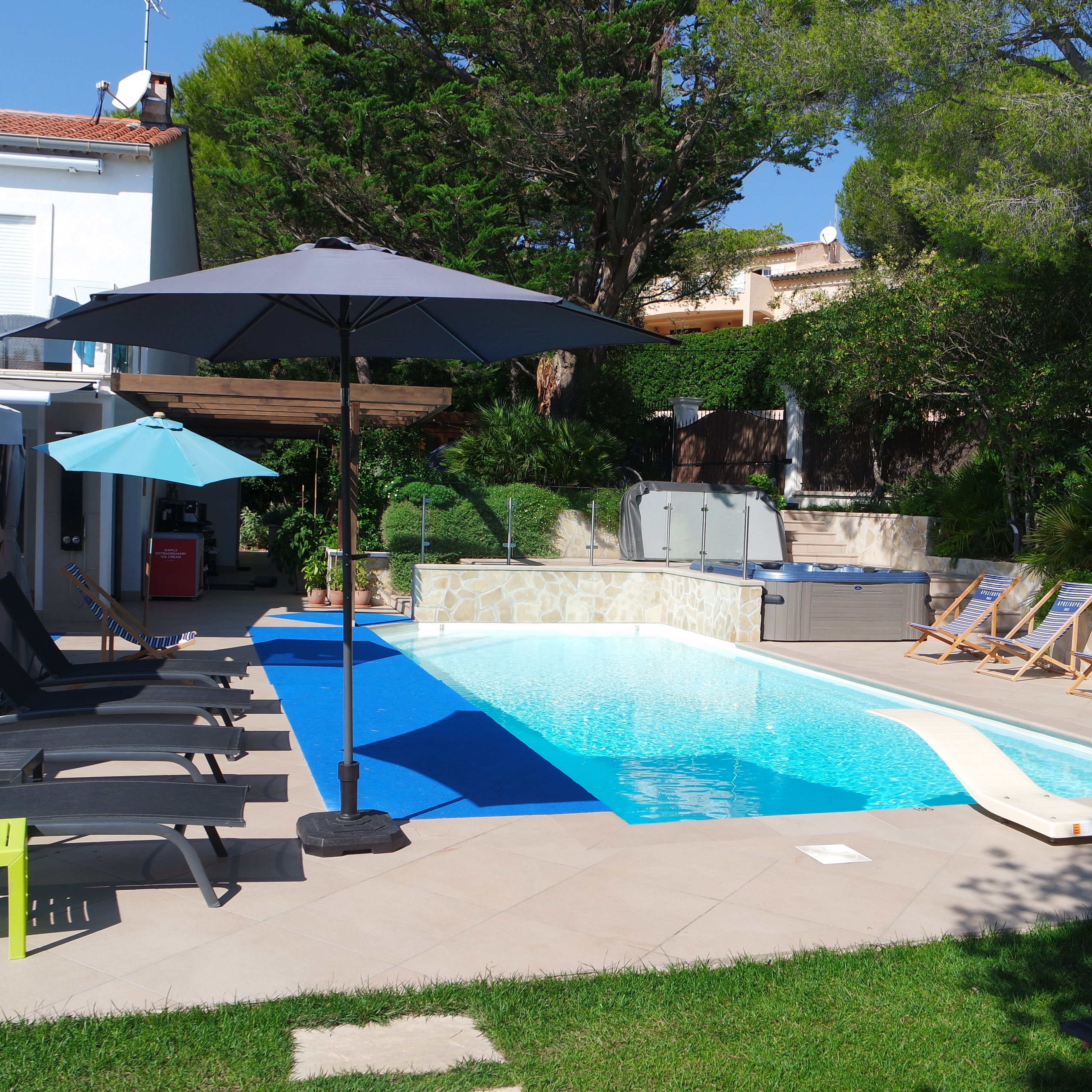 A swimming pool with lounge chairs and umbrellas, surrounded by greenery and a stone wall.