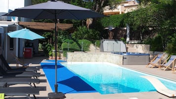 A swimming pool with lounge chairs and umbrellas, surrounded by greenery and a stone wall.