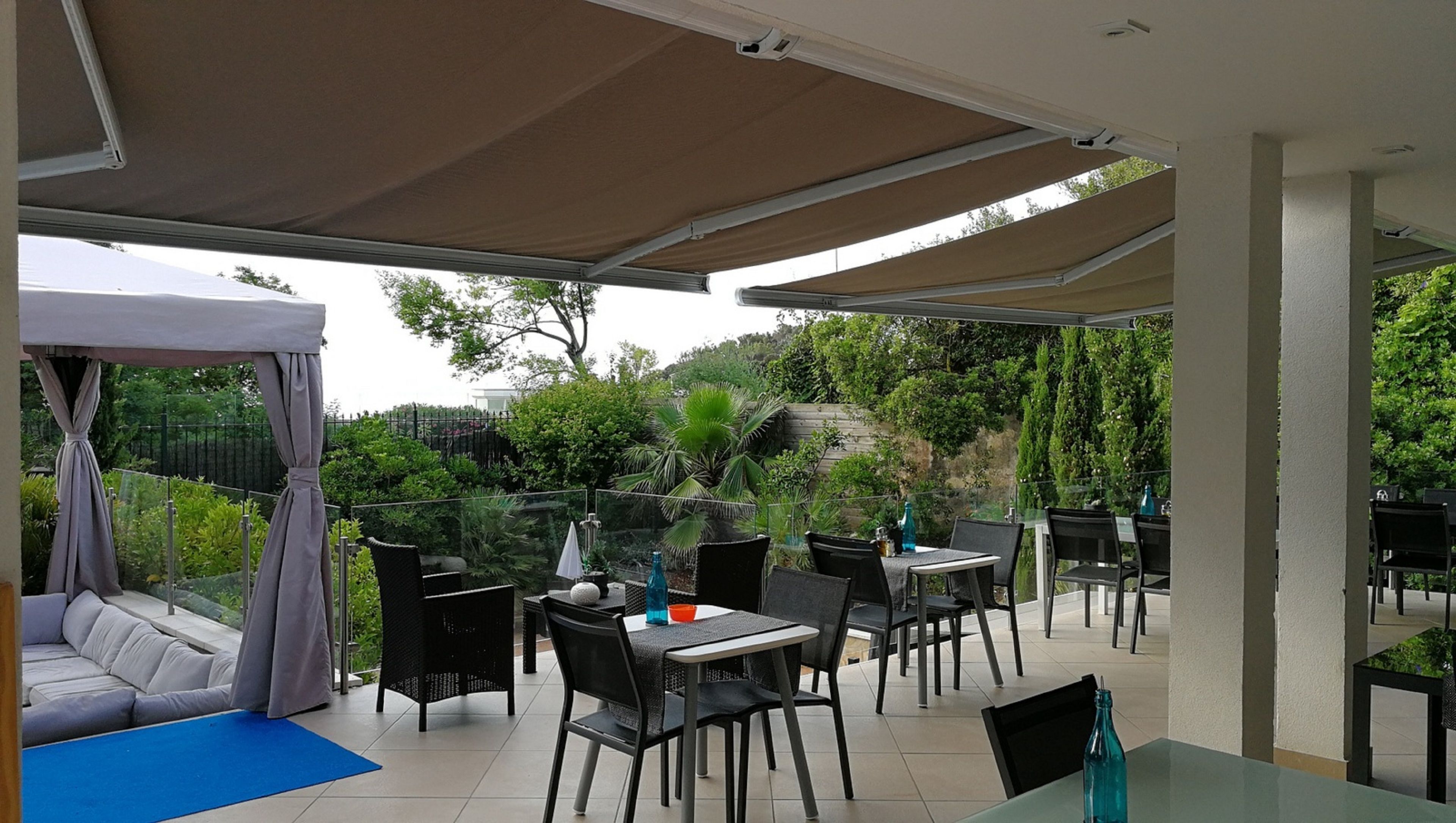 A covered outdoor seating area with tables and chairs, a cushioned sofa, and a pergola with curtains.