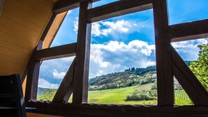 A room with a large window offering a view of a green landscape with hills and trees. - Zum Valwiger Herrenberg (Valwig)
