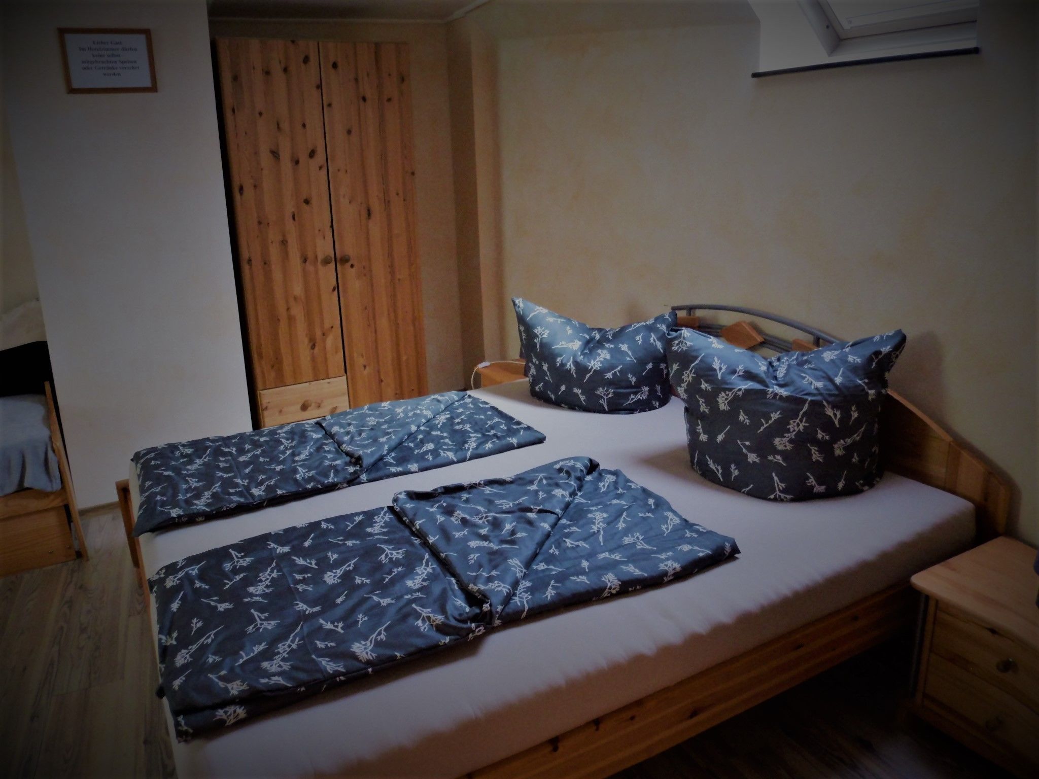 Ein Schlafzimmer mit einem hölzernen Bett, zwei Kissen, einem Nachttisch und einem Kleiderschrank.