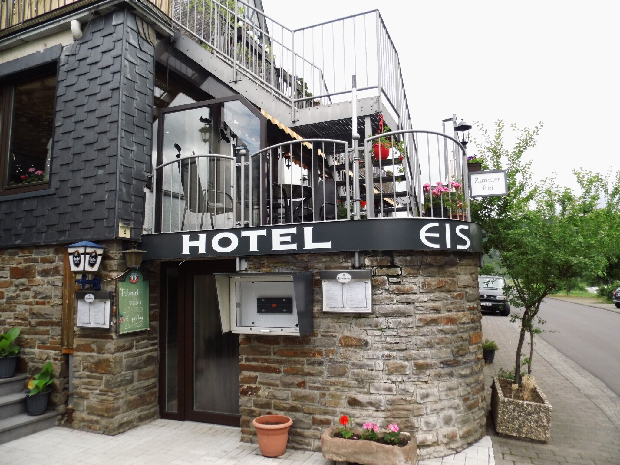 A hotel with a stone facade, a balcony with metal railings, and a sign that reads "HOTEL EIS".