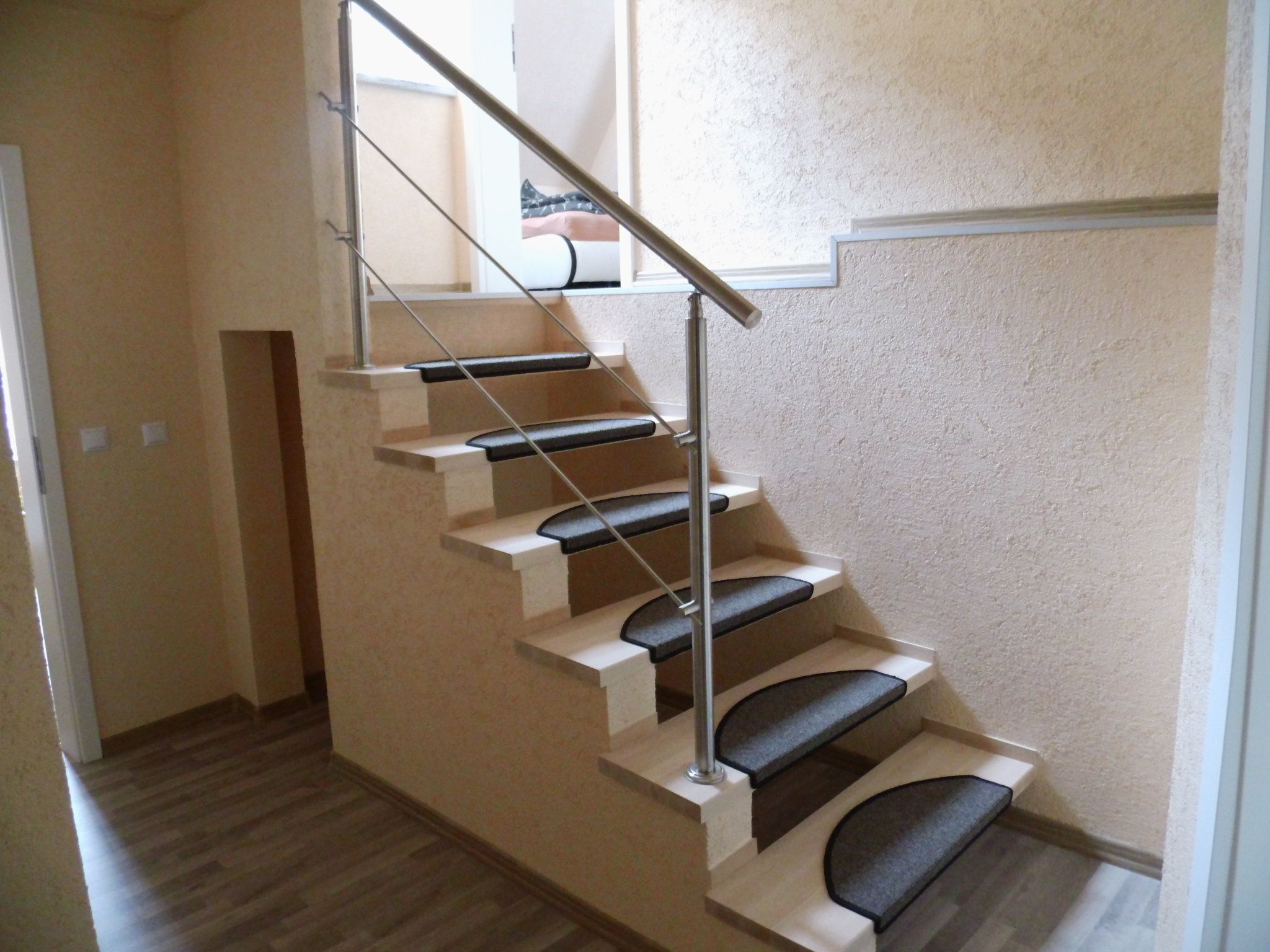 Un intérieur moderne avec un plancher en bois, un mur de couleur beige et un escalier dont les marches sont noires et la rampe est en métal.