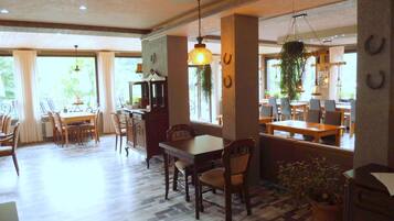 A spacious dining area with a wooden table and chairs, a bar area with a counter, and large windows allowing natural light.
