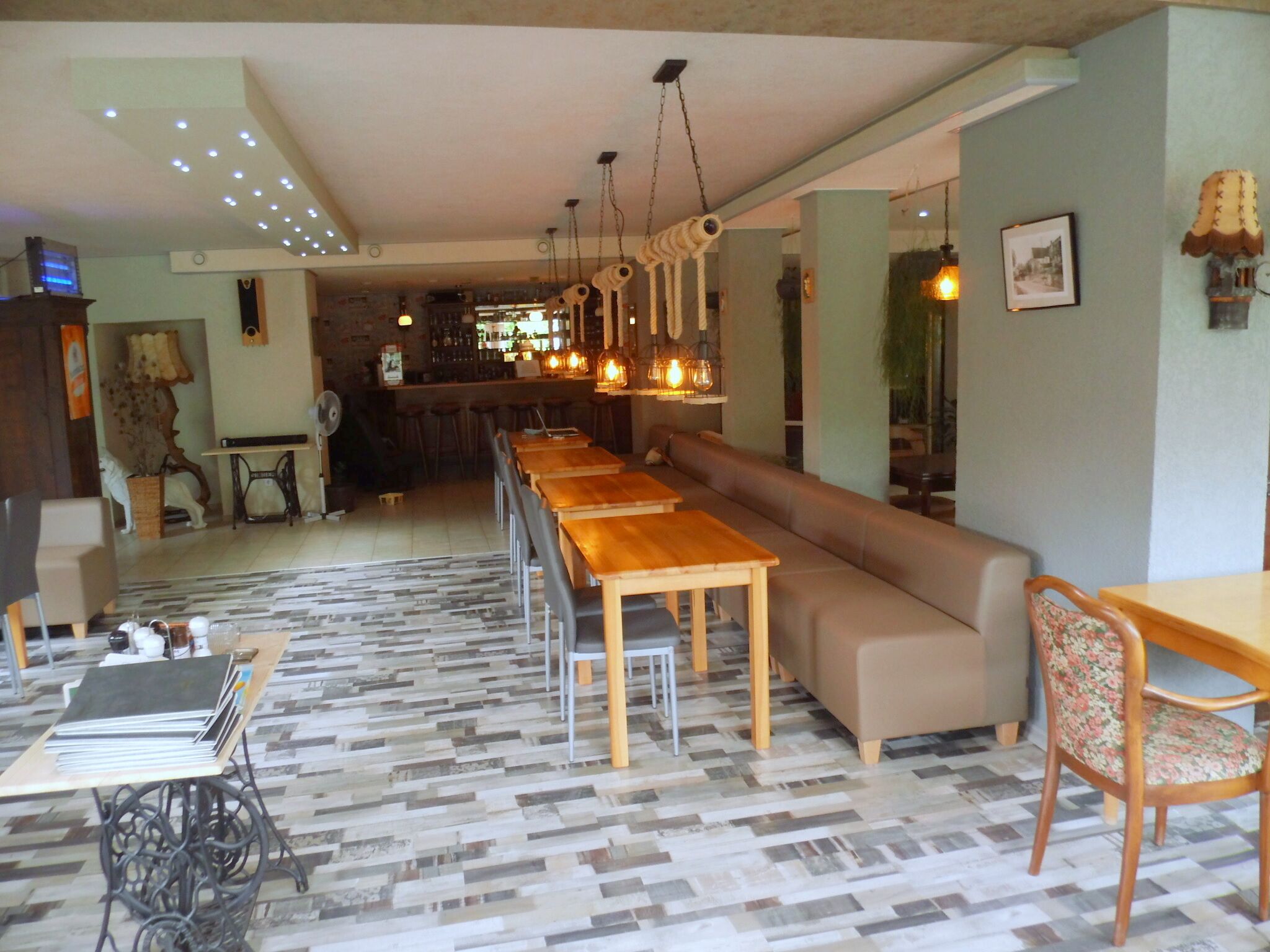 A restaurant with a long wooden table, a sofa, and a bar area in the background.