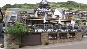 A building with a sign reading "RESTAURANT, CAFE, HOTEL". It has a stone facade, multiple balconies with potted plants, and a staircase leading to the upper floors. - Zum Valwiger Herrenberg (Valwig)