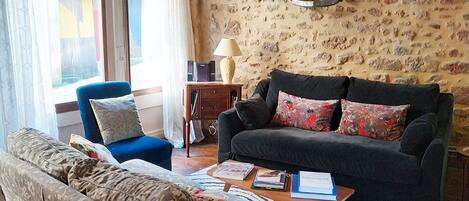 A cozy living room with a sofa, armchair, and a coffee table. There is a stone wall and a wooden ceiling.
