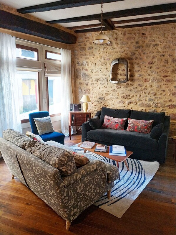 Un salon chaleureux avec un canapé, un fauteuil et une table basse. Il y a un mur en pierre et un plafond en bois.