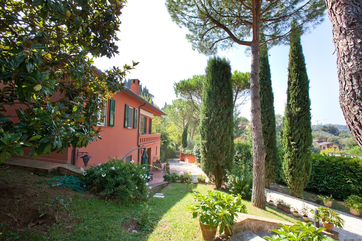 A red building with a garden, including a lawn, potted plants, and tall trees.