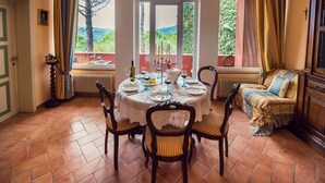 Een eethoek met een ronde tafel gedekt voor vier personen, omringd door houten stoelen met beklede zitplaatsen. Achter de tafel is een raam te zien met uitzicht op groen en heuvels.