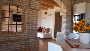 A spacious living area with exposed brick walls, a white sofa, and a dining table with a vase of sunflowers. - I Tre Laghi Sant' Agnese - Rustic with pool, aircon (Pescara)