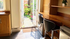 Una cocina con mostrador de madera, dos taburetes negros, un lavamanos de acero inoxidable y un refrigerador pequeño.