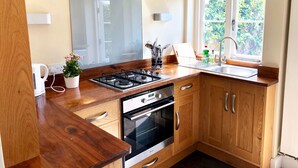 Una cocina moderna con armarios de madera, estufa a gas, horno, fregadero y ventana con vistas al verdor.