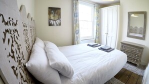 Un dormitorio con una cama grande, un aparador, una ventana con cortinas y un cuadro en la pared.