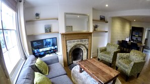 Una sala de estar con chimenea, televisor, sofá y sillones estampados.