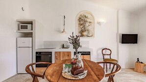 A modern kitchen with white appliances, a wooden dining table with chairs, and a painting on the wall. - Résidence Pietra Di Sole (Porto-Vecchio)