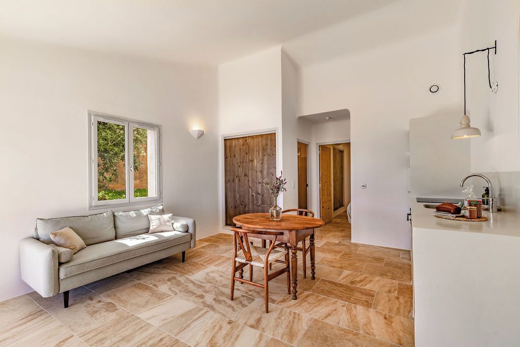 A modern living room with a sofa, a wooden dining table, and a kitchen area with a sink and countertop.
