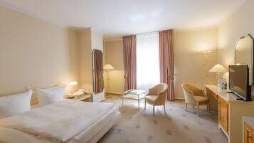 Habitación de hotel con una cama grande, dos sillas, un escritorio con espejo y un televisor.