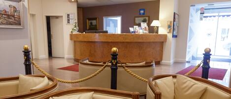 Un hall con mostrador de recepción, sillones de cuero, una mesa redonda de madera y una alfombra roja.