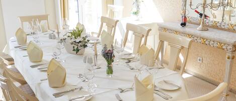 Une salle à manger avec une longue table dressée pour le repas, des chaises, un vase rempli de fleurs et un miroir au mur.