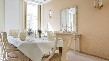 Een eetkamer met een lange tafel gedekt voor een maaltijd, stoelen, een spiegel en een decoratieve wand.
