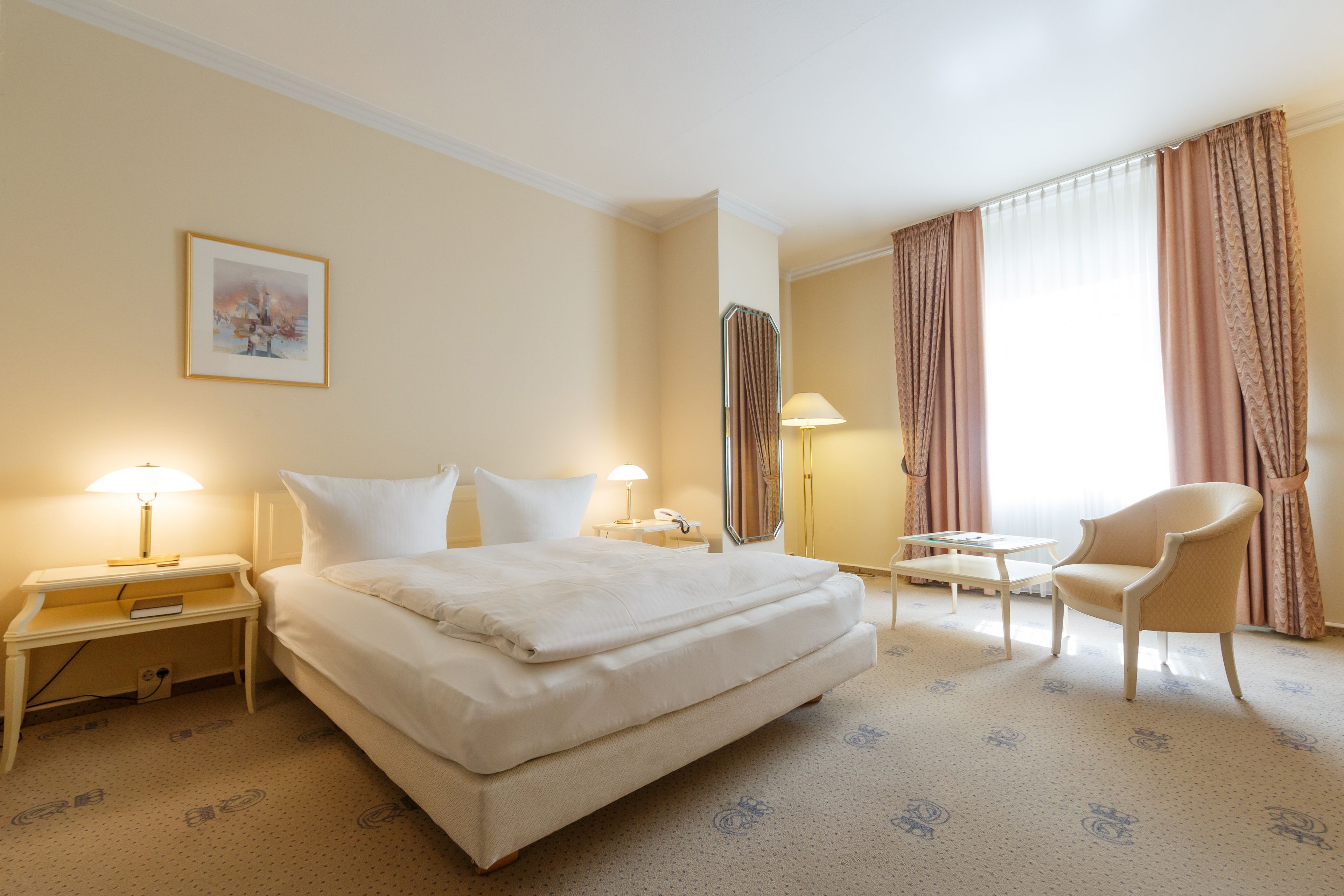 A hotel room with a bed, bedside tables, a chair, a desk, and a lamp.