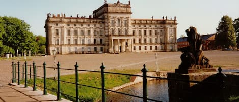 Un edificio grande y histórico con fachada simétrica, un patio central y un canal al frente.