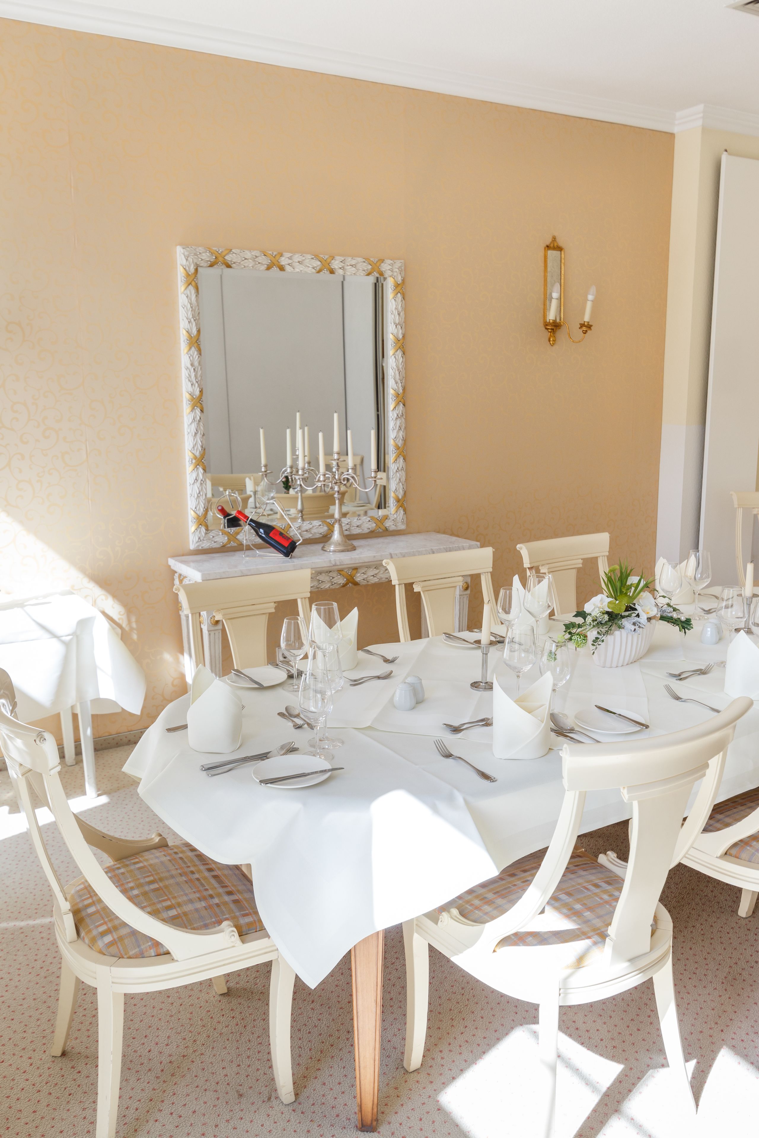 A dining area with a round table set for six, white chairs, and a mirror above the table.