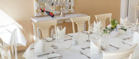A dining area with a round table set for six, white chairs, and a mirror above the table.