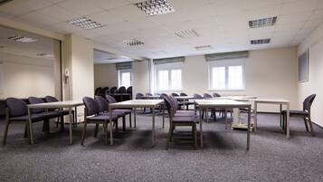 A conference room with multiple tables and chairs, carpeted floor, and windows with blinds.